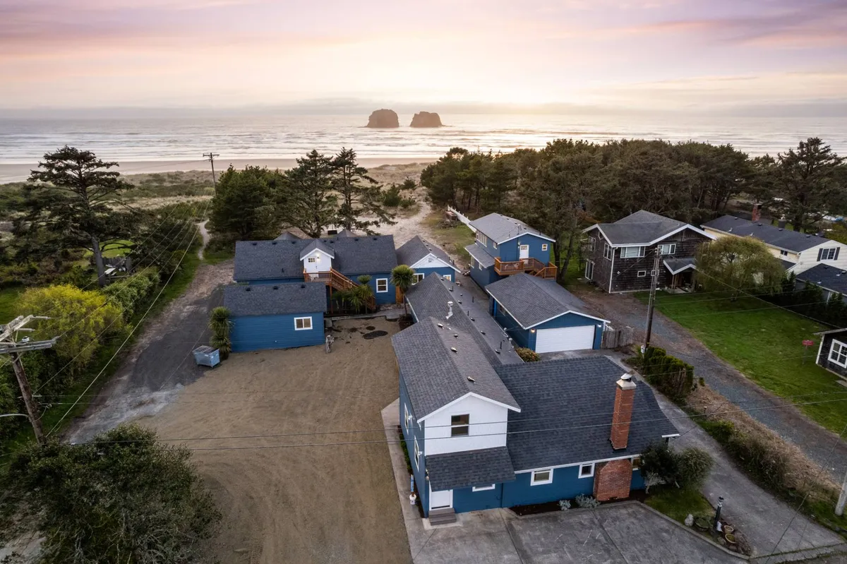 A tranquil exterior scene showcasing an ocean view framed by rock formations, with inviting houses and lush trees nearby. The open yard and coastal backdrop highlight abundant outdoor space for exploration and play.
