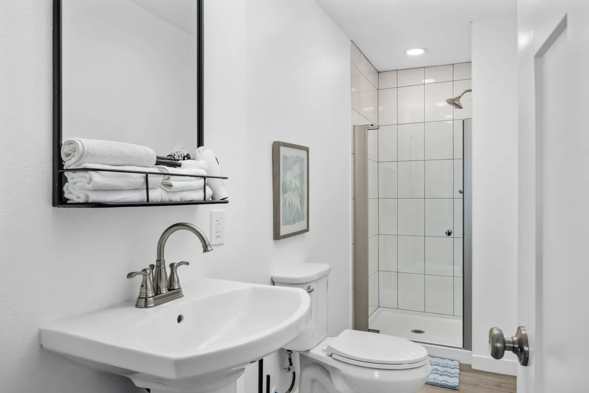 A pristine, modern bathroom with a sleek sink, stylish faucet, neatly folded towels on the shelf, and tasteful framed artwork. The setting feels bright, clean, and inviting—ideal for unwinding after a day by the sea.