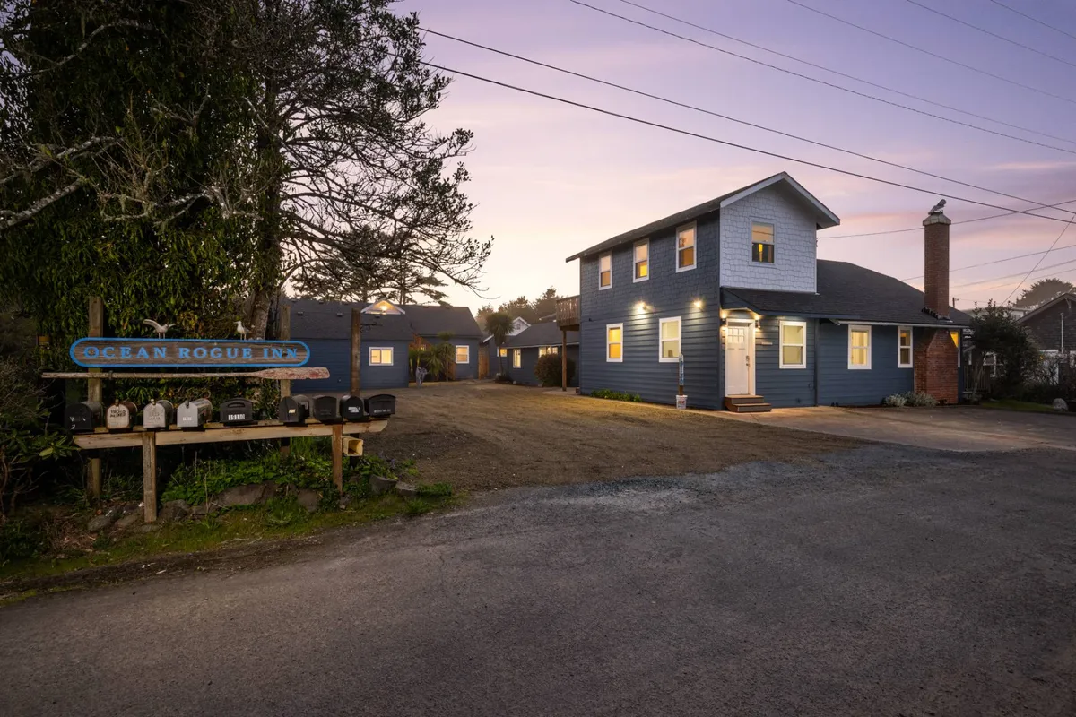 The inviting Ocean Rogue Inn sign stands in front of a charming blue building with a well-maintained yard. The scene highlights the inn as welcoming, with outdoor areas perfect for relaxing or gathering after a day of exploring with pets.