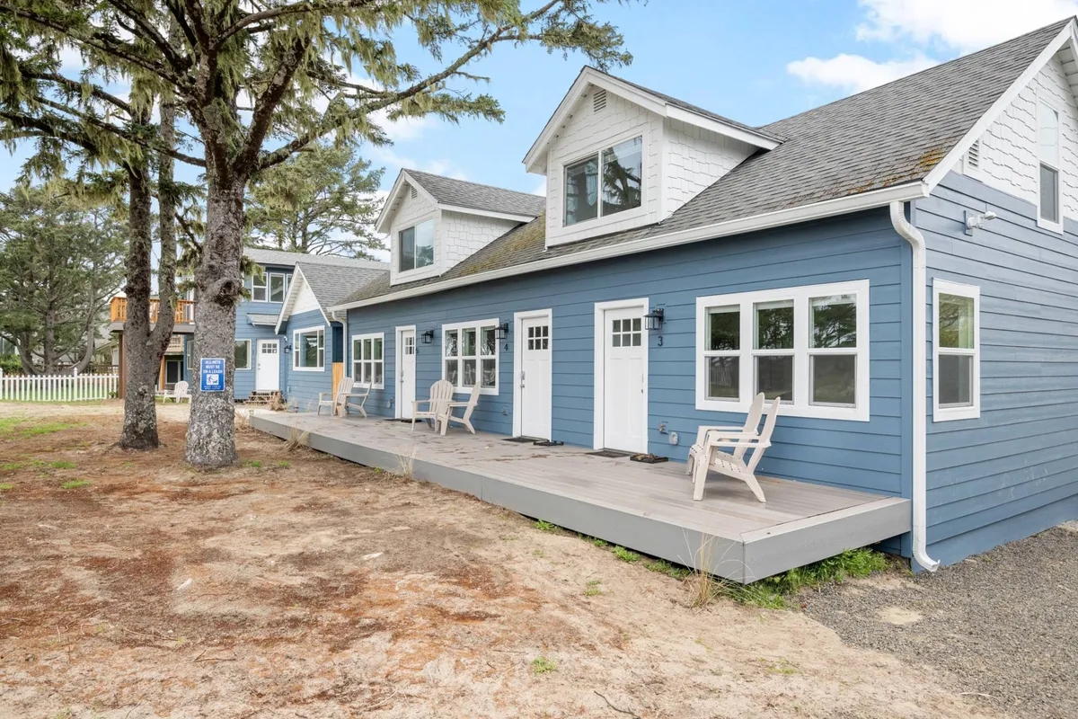 This image shows the blue exterior of the building, front porches with comfortable chairs, and green trees in the background. The porches invite guests to relax outdoors, enjoying coffee in the morning or unwinding after a day in town.