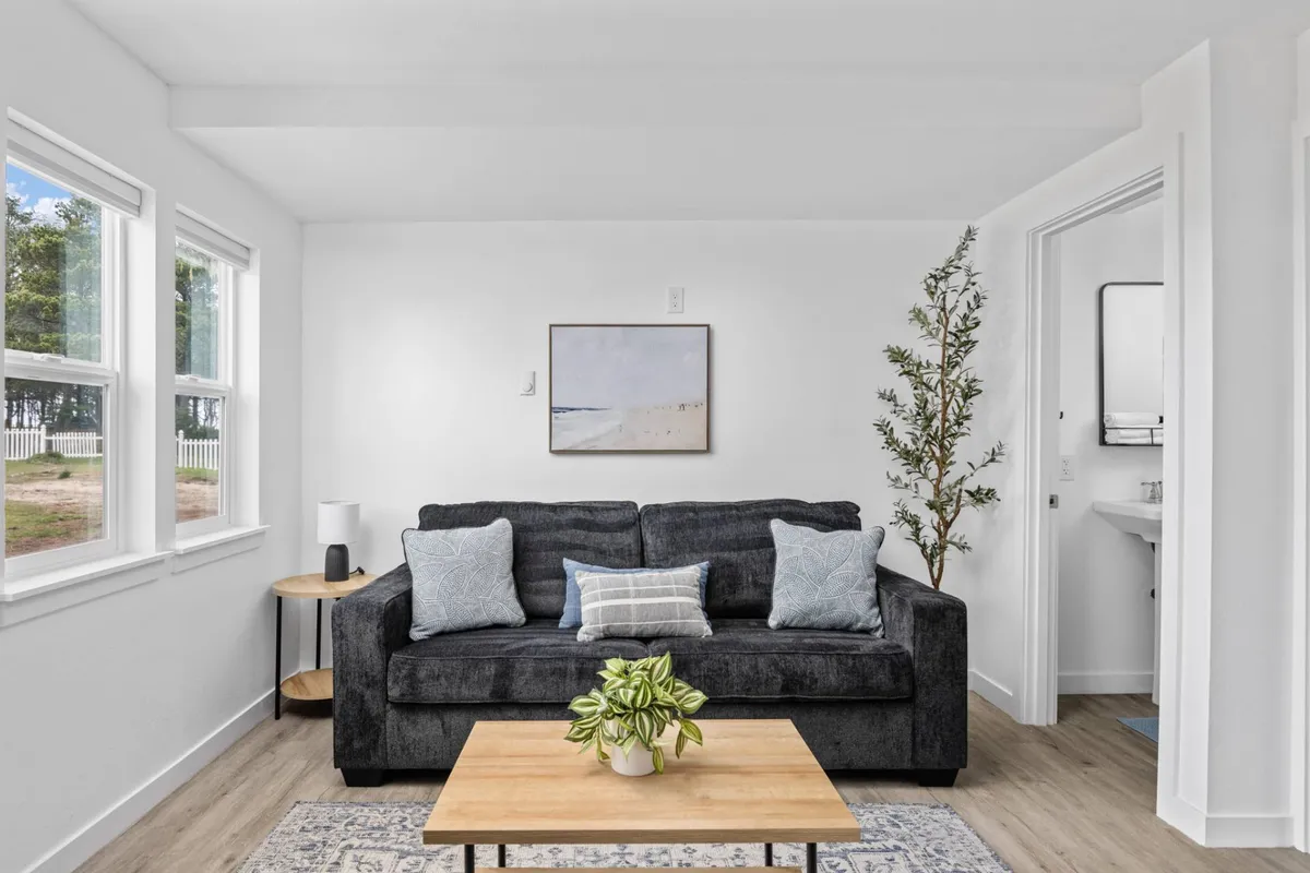 A calm, inviting living room featuring a cozy sofa, a coffee table set for relaxing activities, elegant artwork on the wall, and a lush plant in the corner. The space is uncluttered and comfortable, suggesting a homey environment perfect for families and their pets.