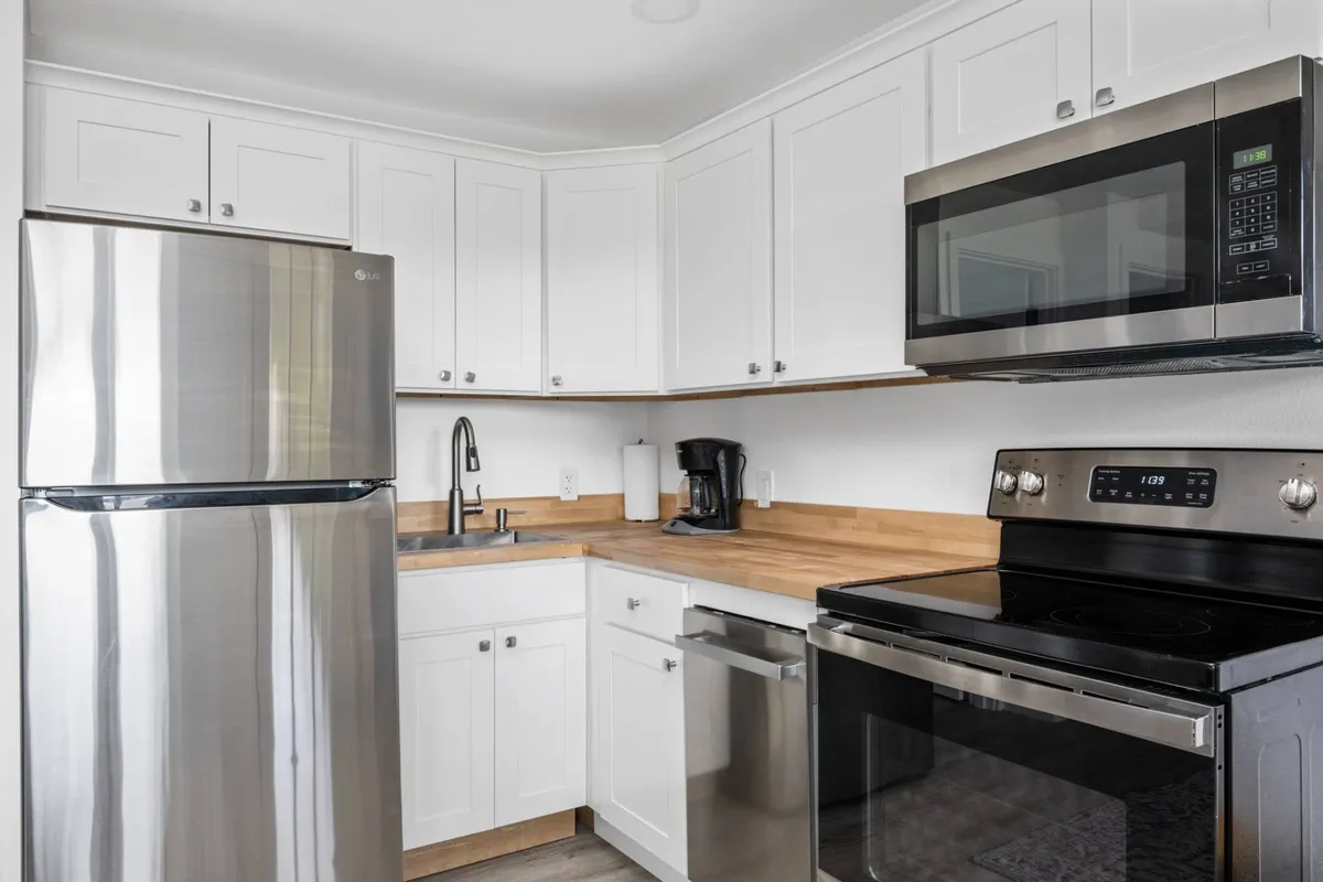 A close-up look at the kitchen area, showcasing stainless steel appliances, a wooden countertop, and white cabinetry. The atmosphere is inviting and functional, reflecting a tastefully remodeled space ideal for preparing seaside meals or gathering with friends and family.