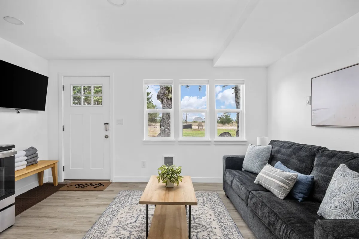 The image showcases the inviting living area of the condo, featuring a plush sofa and coffee table set before large windows that fill the room with natural light. The windows offer tranquil views and create a cozy, welcoming atmosphere perfect for relaxation, social gatherings, or quiet mornings with coffee.