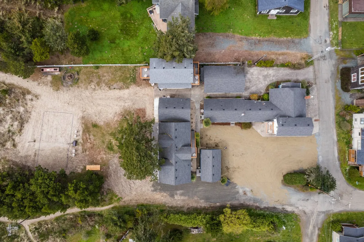 This image highlights a cluster of buildings surrounded by lush greenery and a dirt path, with open outdoor areas suitable for group activities. The peaceful setting is ideal for showcasing shared outdoor amenities such as a sand volleyball court or communal gathering spaces.