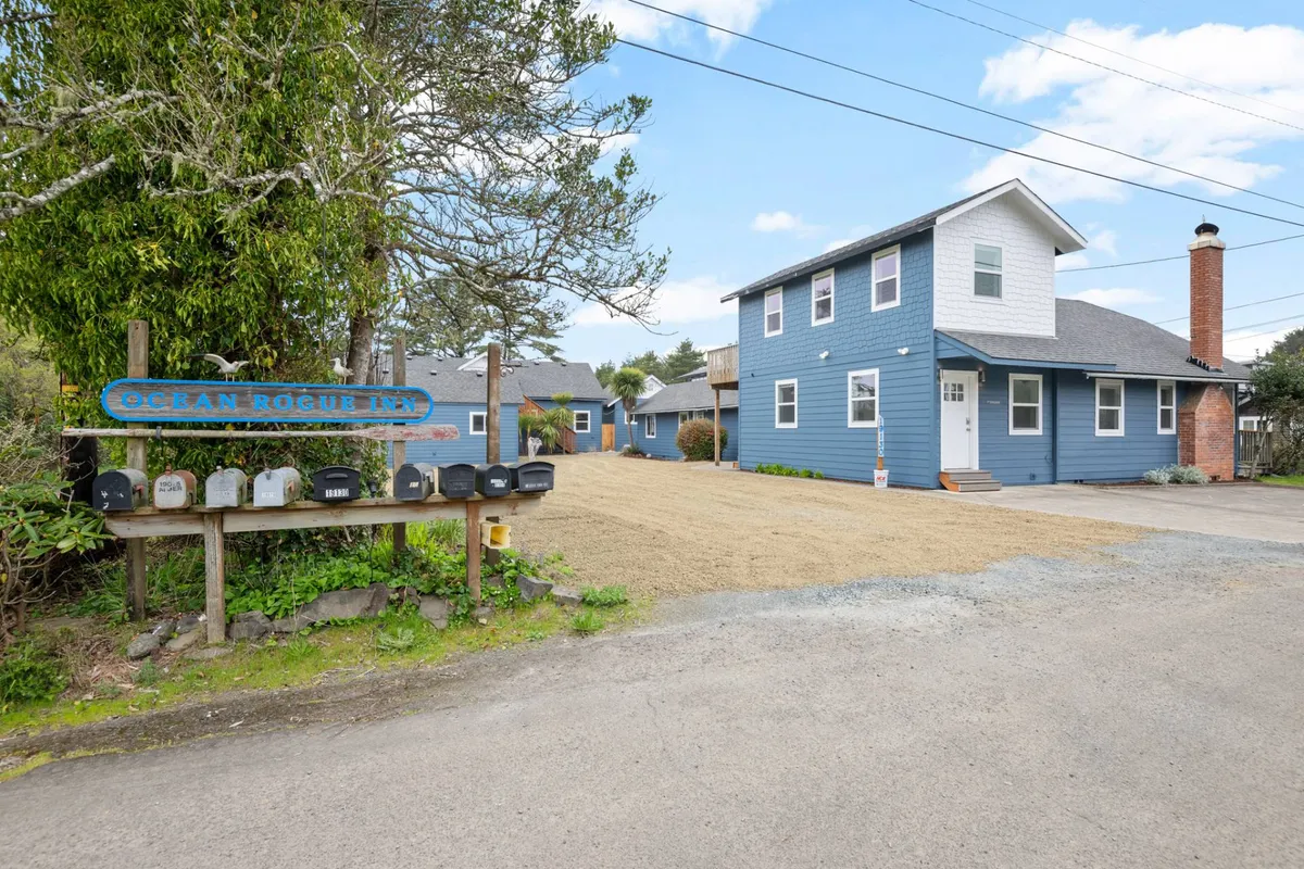 A wide-angle view of the inn’s exterior, featuring the prominent blue siding, welcoming signage, and a mailbox area edged with lush greenery. The image hints at community interaction and the inn’s approachable, friendly spirit.